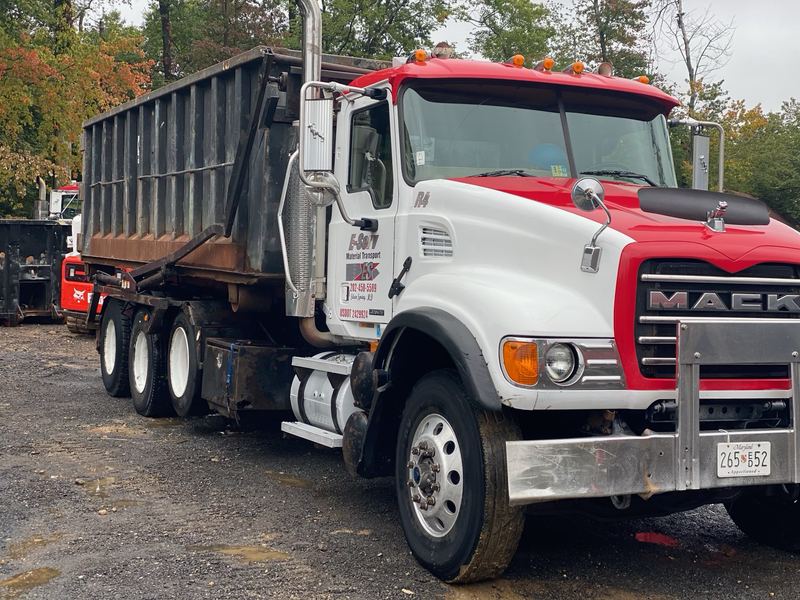 Front view of a white and red Mack roll-off truck with a dumpster on the back
