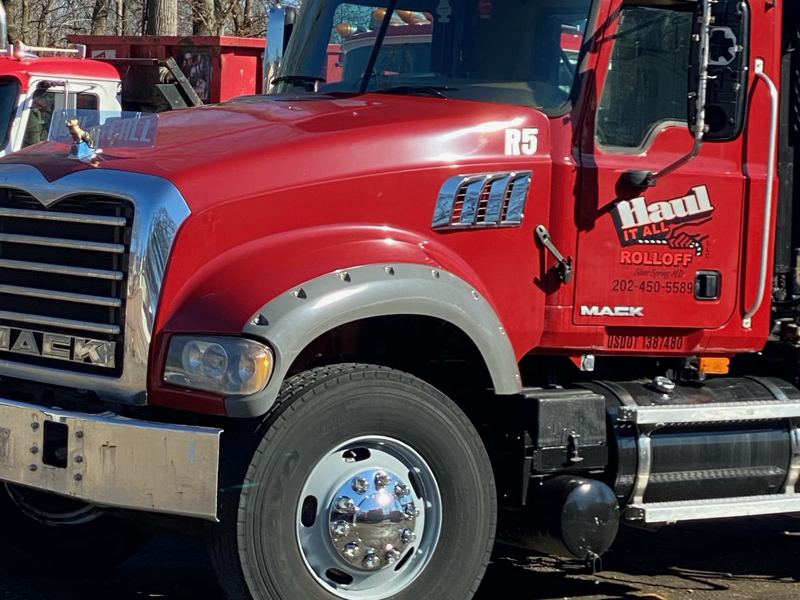 Red Mack roll-off truck cab with Haul It All Rolloff lettering and 202-450-5589 on the door